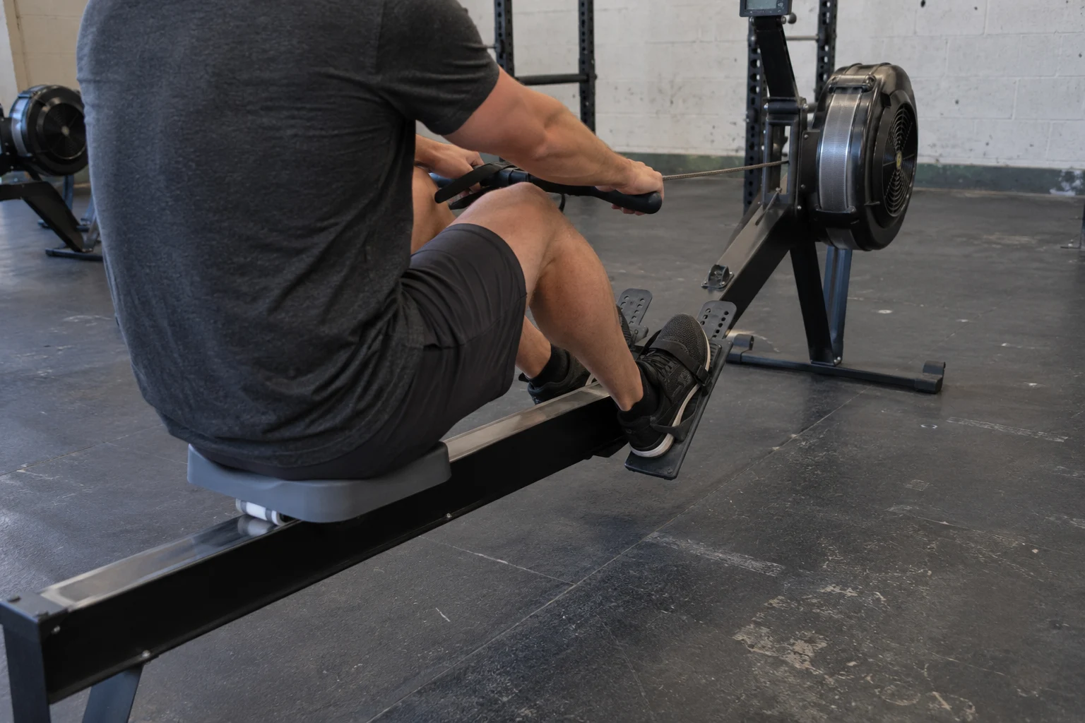A rower seen from behind on an air-resistance rowing machine in a worn community gym