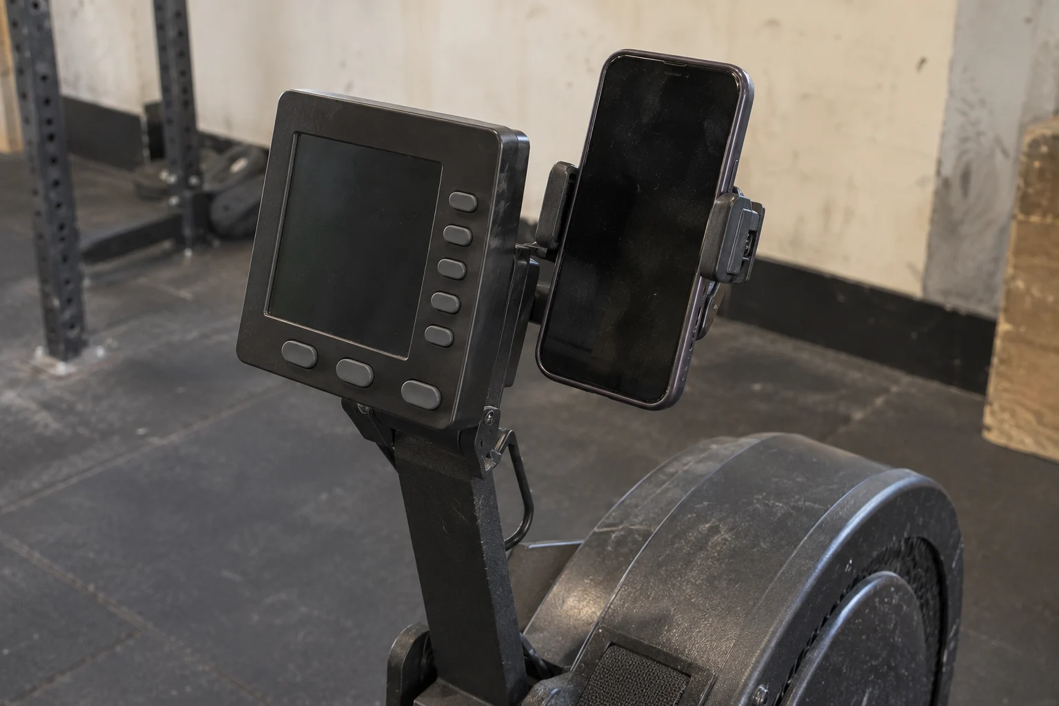 A dark-screen phone held beside a rowing monitor on a worn equipment arm
