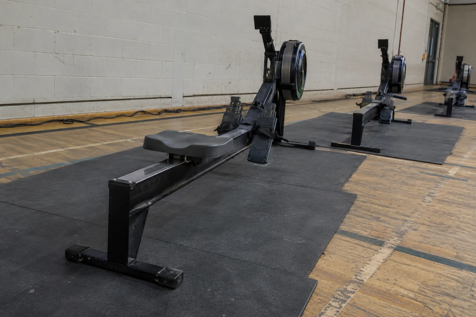 Indoor rowing machines positioned diagonally on rubber mats in a sports hall