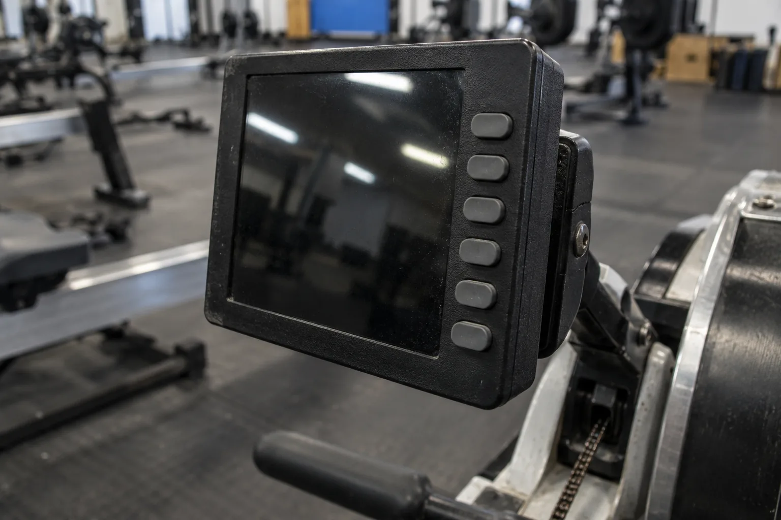 Close-up of a dark indoor rowing performance monitor and its right-hand column of physical buttons in a community gym